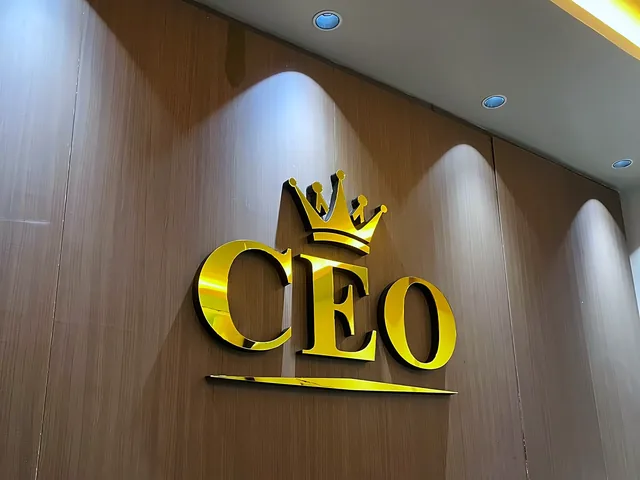 Gold dimensional CEO letters under a crown, mounted on a timber-panelled wall.